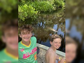 Two children pose for a photo while enjoying a close encounter with an alligator in the background, showcasing the thrill of wildlife experiences.