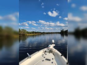 A serene view from the front of a boat cruising on calm waters, surrounded by lush greenery and a clear blue sky — perfect for a peaceful day on the water.