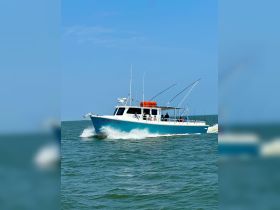 A fishing boat cruises through the water, with guests onboard enjoying the experience — perfect for a day of fishing adventures.