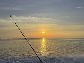 A serene sunset view over calm waters with a fishing rod in the foreground, capturing the essence of a peaceful fishing trip.