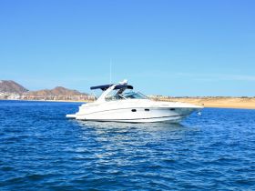 A sleek yacht cruising through clear blue waters, showcasing its elegant design against a backdrop of coastal hills and a vibrant shoreline.