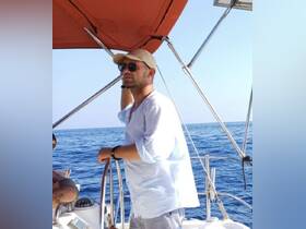 A man stands at the helm of a sailboat, enjoying a sunny day on the ocean — perfect for sailing adventures and exploring the open waters.