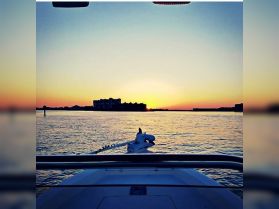 A serene sunset view from the bow of a boat, showcasing the tranquil waters and silhouetted buildings in the background — perfect for evening cruises.