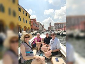 A cheerful group enjoys a scenic boat ride through a picturesque canal, surrounded by colorful buildings — a perfect way to explore the charming waterways.