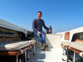 A man relaxes inside the cabin of a boat, showcasing the comfortable seating and helm area — perfect for enjoying a day on the water.
