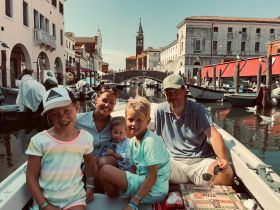 A cheerful family enjoys a scenic boat ride through a picturesque canal, surrounded by charming architecture and vibrant scenery — a perfect vacation experience.