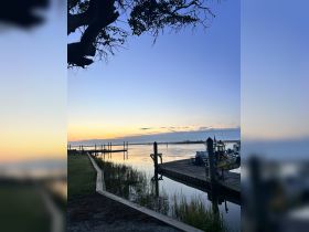 A serene view of a dock at sunset, with reflections on the water and a hint of boats in the distance, creating a tranquil atmosphere.