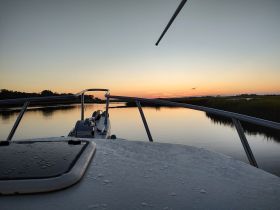 A serene view from the front of a boat at sunset, reflecting calm waters and lush greenery — perfect for peaceful evening cruises.