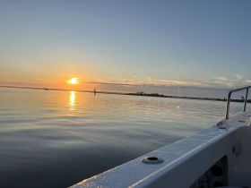 A serene sunset view from the side of a boat, capturing the tranquil waters and distant shoreline — perfect for peaceful evening cruises.
