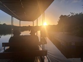 Two individuals enjoy a serene sunset view from their boat, with a picturesque dock in the background — a perfect moment for relaxation on the water.