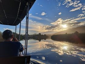 A serene sunset view from a boat, capturing the reflection on the river as a guest enjoys the tranquil scenery — perfect for peaceful evening cruises.