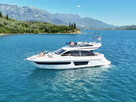 A couple relaxes on the deck of a luxurious yacht cruising through stunning turquoise waters, surrounded by picturesque mountains — an ideal setting for a romantic getaway.