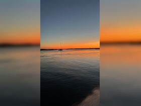 A serene sunset view featuring a sailboat gliding across calm waters, perfect for capturing the tranquility of evening boat outings.