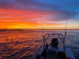 A stunning sunset view from the back of a fishing boat, showcasing vibrant colors reflecting off the water — perfect for evening fishing trips.