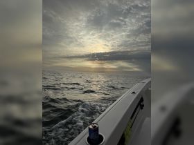 A serene view of a boat's edge with a can resting in the holder, set against a dramatic sunset sky over the ocean — perfect for capturing the tranquility of a boating experience.