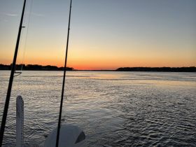 A serene sunset view from a boat, showcasing the tranquil waters and silhouettes of the shoreline — perfect for evening cruises.