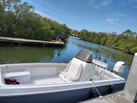 A sleek speedboat is docked near a wooden pier, with fishing rods visible, set against a backdrop of lush greenery — perfect for a day of fishing adventures.