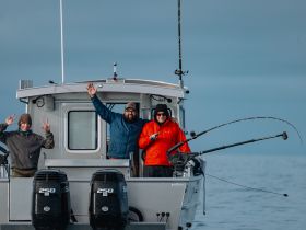 A cheerful group of friends enjoys a fishing trip on a boat, showcasing their excitement with waves and smiles — perfect for adventure seekers and fishing enthusiasts.