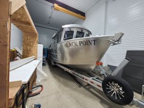 An interior view of a boat named 'Black Point' stored in a garage, showcasing its sleek aluminum design and trailer setup.