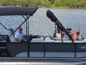 A cheerful group waves from a pontoon boat, enjoying a sunny day on the water — perfect for family outings and fun adventures.