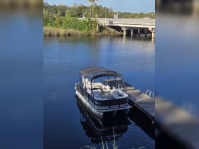 A serene view of a pontoon boat docked by the shore, surrounded by tranquil waters and lush greenery, perfect for a relaxing day on the water.