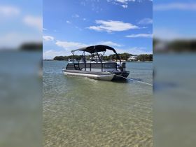 A sleek pontoon boat anchored in shallow waters, showcasing its modern design against a clear blue sky — perfect for leisurely outings or family gatherings.
