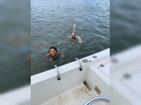 A joyful moment captured as a child and an adult swim together in clear waters, showcasing the fun of a day on the boat.