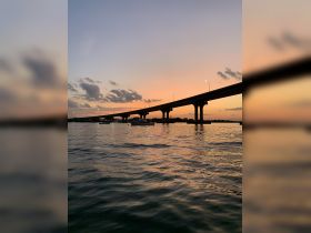 A stunning sunset view featuring a bridge silhouetted against the colorful sky, reflecting beautifully on the water — a perfect scene for evening boat trips.