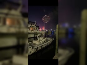 A stunning view of fireworks lighting up the night sky above a marina, with boats docked and a festive atmosphere — perfect for celebrating special occasions.