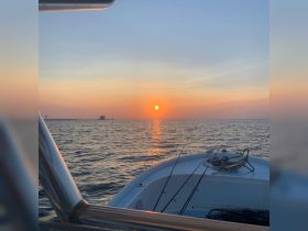 A serene sunset view from the bow of a fishing boat, showcasing the tranquil waters and a hint of the coastline — perfect for evening fishing trips.
