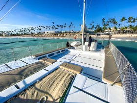 A stunning view of a catamaran's deck with a backdrop of palm trees and a beach, showcasing the perfect setting for a day on the water.