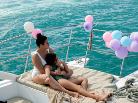 A mother and child relax together on a boat adorned with colorful balloons, capturing a joyful family moment on the water.