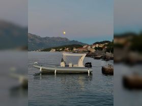 A serene view of a speedboat docked in calm waters, with a picturesque backdrop of mountains and a rising moon, perfect for evening cruises.