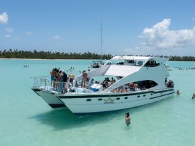 A lively group enjoys a sandbar stop, with guests swimming and socializing around a spacious boat in crystal-clear waters — the perfect setting for a fun day on the water.