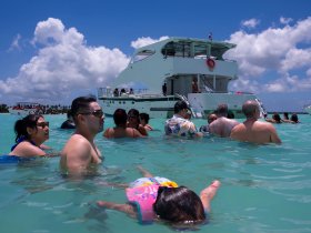 A lively group enjoys a fun day in the water, swimming around a boat in beautiful aquamarine waters — perfect for summer parties and family outings.