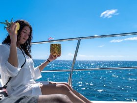 A woman enjoys a refreshing pineapple cocktail while relaxing on a boat, surrounded by the sparkling ocean under a clear blue sky — a perfect moment for leisure and enjoyment on the water.