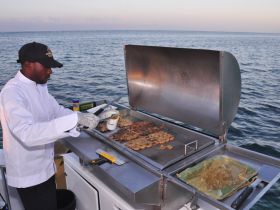 A chef prepares fresh seafood on a grill aboard a boat, showcasing the culinary amenities available for an unforgettable dining experience on the water.