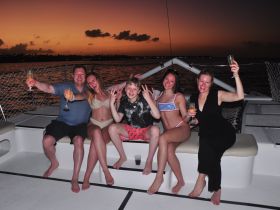 A joyful group celebrates at sunset on a boat, raising their glasses for a memorable evening — perfect for family gatherings or special occasions on the water.