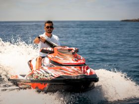 A man rides a vibrant jet ski, creating splashes in the open water — a thrilling moment showcasing the excitement of water sports.