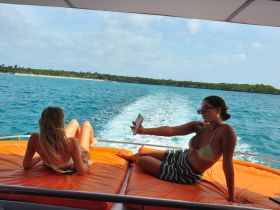 Two friends enjoy a sunny day on a boat, capturing the moment with a selfie while relaxing on the deck — a perfect snapshot of fun on the water.