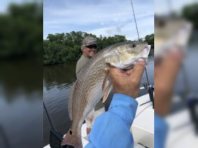 A successful fishing trip captures a proud angler holding up a freshly caught fish, with a scenic backdrop and fellow fisherman enjoying the day on the water.