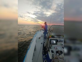 A fisherman casts his line into the ocean at sunset, capturing the serene beauty of a fishing trip on the water.