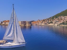 A picturesque view of a sailboat gliding through calm waters, with a charming coastal town in the background, perfect for showcasing sailing adventures in scenic destinations.