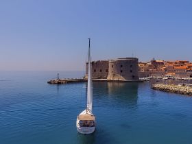 A picturesque sailboat navigates the calm waters near a historic coastal fort, showcasing the beauty of sailing in scenic destinations.