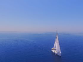 An aerial view of a sailboat gracefully gliding across calm blue waters, showcasing the serene beauty of sailing.