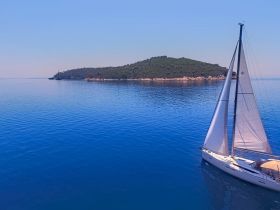 A stunning aerial view of a sailboat gliding through calm waters, with a picturesque island in the background — perfect for showcasing serene sailing adventures.