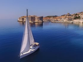 A stunning aerial view of a sailboat gliding through calm waters near a historic coastal town, showcasing the beauty of sailing and scenic destinations.