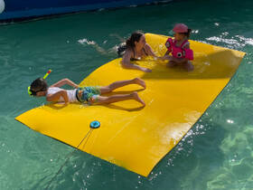 A joyful scene of children enjoying a sunny day on a floating mat in clear waters, perfect for family fun and aquatic adventures.