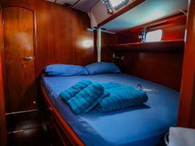 Cozy interior cabin of a boat featuring a comfortable bed with blue linens and towels, perfect for relaxing during a sailing trip.
