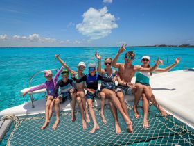 A joyful group of kids and teens celebrate on the deck of a catamaran, enjoying the stunning turquoise waters — a perfect day of fun in the sun.